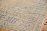 Distressed Oushak rug corner showing faded beige, denim blue, pink floral motifs, visible wear.