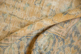 Textured pile and rolled edge of a distressed Oushak carpet in soft gold, beige, and muted blue.