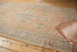 Distressed Oushak carpet corner with pale apricot, blue, green floral motifs and aged texture.