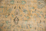 Distressed Oushak carpet close-up, featuring faded floral vinery in beige, mint, and muted pink.