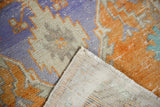Distressed Oushak rug showing textured pile in lavender, tangerine, and grey with hand-knotted foundation.