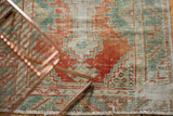 Distressed Oushak rug corner showing vivid rust, seafoam green, and geometric motifs.