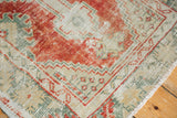 Distressed vintage Oushak rug corner in rust red, mint green, and ivory with fringe.