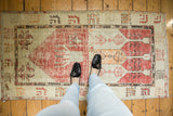 Distressed Oushak rug corner showcasing pale cherry red field with geometric motifs and textural wear.