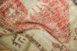 Distressed vintage rug pile, showcasing faded cherry red, ivory, and charcoal brown motifs.