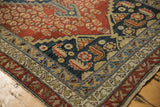Antique Malayer rug corner showing madder red field, navy design, and detailed beige borders with wear.