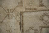 Folded corner of distressed Oushak carpet, showing low pile, secured edge, and brown motif.