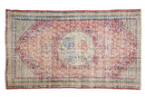 Vintage distressed Oushak rug with a red and blue floral medallion on a worn, sand-colored field.