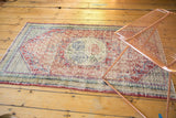 Angled view of a vintage Oushak rug highlights its distressed texture and faded cherry red and indigo blue medallion.