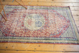 Angled view of a distressed Turkish Oushak rug showcasing the faded cherry red field and heavily worn texture.