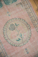 Vintage distressed Oushak rug close-up showing worn pink pile, ivory roundel medallion, green rose stem.
