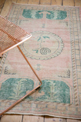 Distressed pink Oushak runner's worn pile and green laurel end motif.