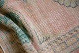 Evenly worn knot heads with faded pink, forest green, and ivory on a distressed Oushak rug.