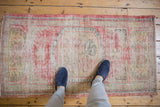 Distressed vintage Oushak runner with faded cherry red, beige, and visible wear.