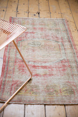 Corner view of distressed vintage Oushak rug, with soft red hues and visible foundation.