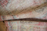 Distressed Oushak rug showing even wear, visible foundation, muted cherry red and beige.