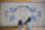 Distressed vintage Oushak rug corner showing cobalt blue Rococo scrolling and ivory field with even wear.