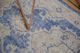 Distressed Oushak rug texture with worn cobalt blue and dusty rose scrolling motifs.