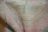 Vintage distressed Oushak rug texture with worn knot heads, faded pink and seafoam green.