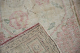 Vintage distressed Oushak rug with dusty rose floral motif and visible hand-knotted foundation.