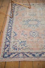 Distressed Oushak rug corner with dusty rose field and cobalt blue geometric border.