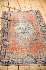 Distressed Turkish Oushak rug showing worn texture, cobalt blue vinery, terra cotta field.