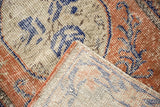 Distressed Oushak rug's folded corner, revealing worn pile texture and dusty rust, blue, ivory.