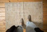 Feet on a distressed vintage Oushak rug, showing worn pile and neutral patterns.