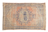 Distressed vintage Oushak rug featuring a faded blush field and blue medallion with scrolling vinery.