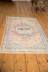 Distressed Oushak rug showing faded cobalt vinery on dusty blush, with even wear and faint foundation.
