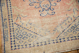Distressed Oushak rug corner with faded blue geometric and curvilinear motifs.