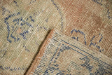 Distressed Oushak rug texture showing mostly even wear to knot heads, secured edge, faded blue and blush tones.