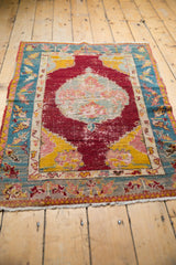 Angled view of an antique Anatolian rug with a worn red medallion and bright saffron spandrels.