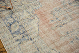 Distressed Oushak rug detail showing faded blush, ivory, and blue floral motifs with visible foundation.