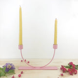 Pink U-shape candlestick holder displaying two yellow taper candles.