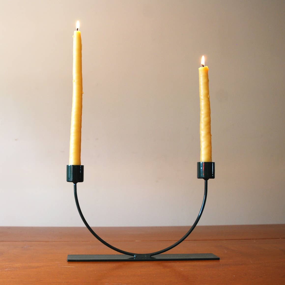 Modern black U-shape candlestick holder holding two lit yellow taper candles.