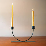 Modern black U-shape candlestick holder holding two lit yellow taper candles.