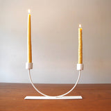 Modern cream U-shape candlestick holder displaying two lit yellow taper candles.