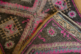 Distressed pile texture and vivid pink geometric patterns on a folded Oushak rug mat.