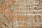 Distressed Oushak rug's worn pile, revealing foundation and beige, sand, and terra cotta tones.