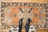 Distressed Oushak rug corner with tangerine, ivory, green, and brown serrated leaf motif.