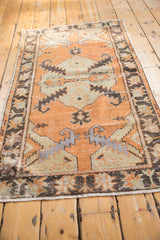 Distressed Oushak rug runner's lower corner, with charcoal border motifs and worn ivory fringe.