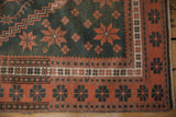 Distressed Oushak rug corner showing faded teal field and terra cotta floral cross-sections.