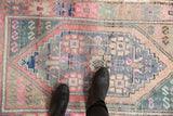 Distressed Oushak rug showing worn pile, pink, blue, and beige tones of its medallion.