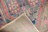 Folded distressed Oushak rug, revealing worn pink, blue, green pile and light foundation.