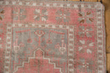 Distressed Oushak rug corner with dusty blush and silver plant motifs, geometric border.