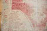 Distressed Oushak rug corner, showing worn cherry red patterns and ivory foundation.