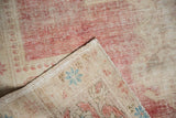 Vintage distressed Oushak rug corner revealing worn red pile, beige foundation, blue motifs.