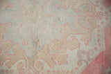 Oushak rug's distressed low pile shows curvilinear pearl design in rose, ivory, and beige.