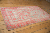 Distressed vintage Oushak rug corner showing pale raspberry and silver slate floral borders, with secured edge.